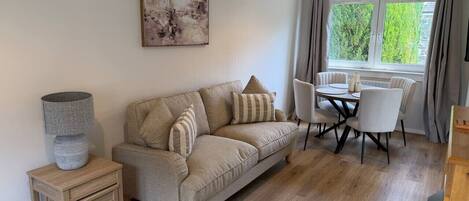 A living room with a sofa, a table with chairs, a lamp, and a painting on the wall.