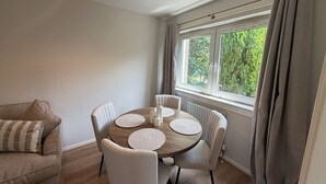 A dining area with a round table, white chairs, and a window with curtains. - The Narrows - Macaulay Letting (Rhu)