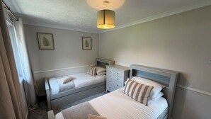 A bedroom with two single beds, a dresser, a bedside table, and a hanging light fixture. - The Narrows - Macaulay Letting (Rhu)