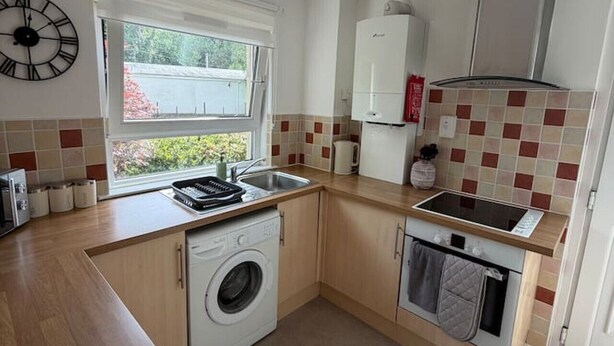 A compact kitchen with a washing machine, a stove, and a sink. - The Narrows - Macaulay Letting (Rhu)