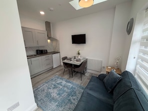 Een compacte leefruimte met een kitchenette, een eethoek en een zithoek met een bank.