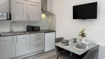 A modern kitchen with a built-in microwave, toaster, and coffee maker, a dining area with a table and chairs, and a flat-screen TV mounted on the wall.