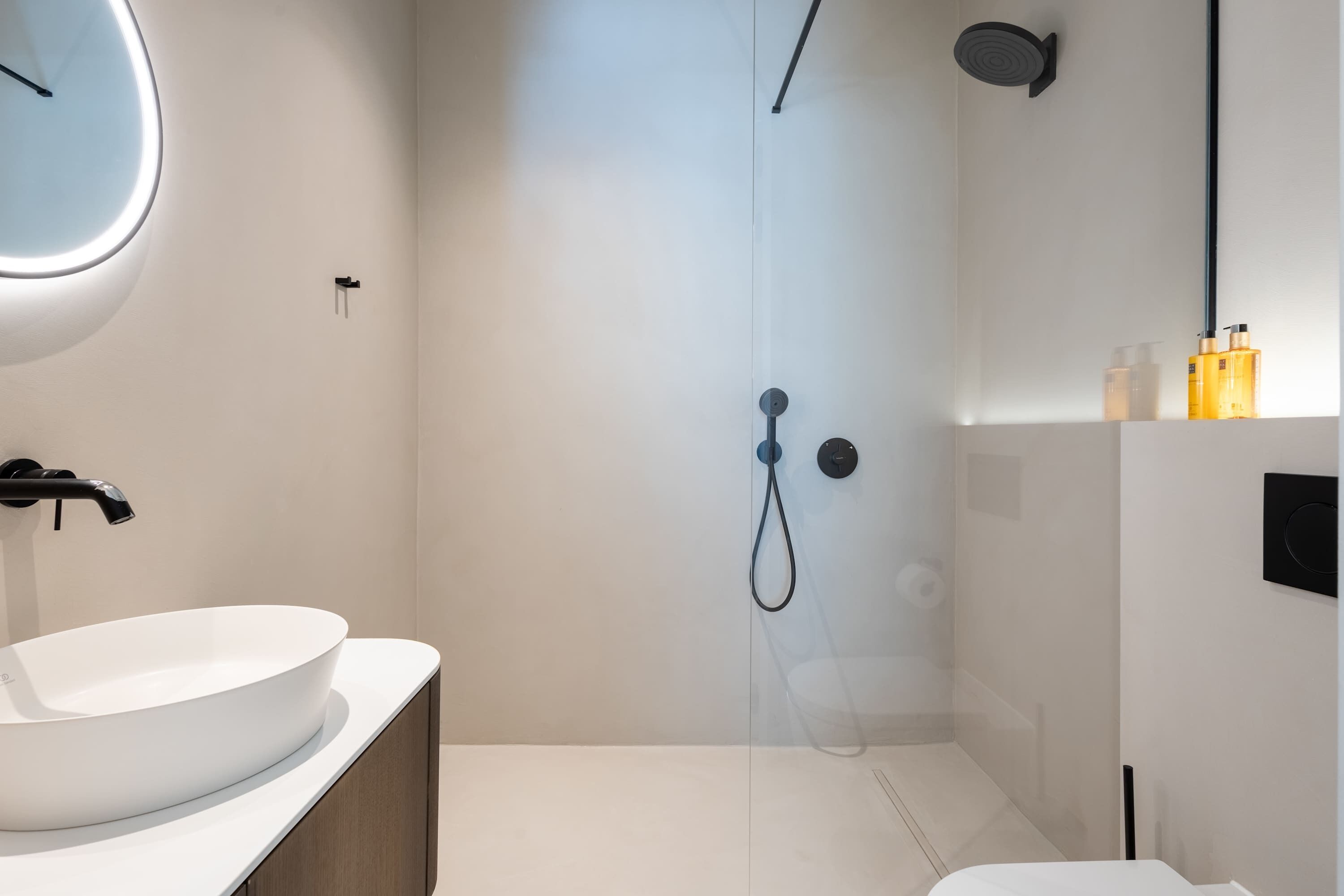A modern bathroom with a large white sink, a shower with a handheld showerhead, and a toilet.