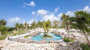 A pool area with multiple seating arrangements and palm trees. - Private Pool Escape - Luminara at The Reef (Sint Michiel)
