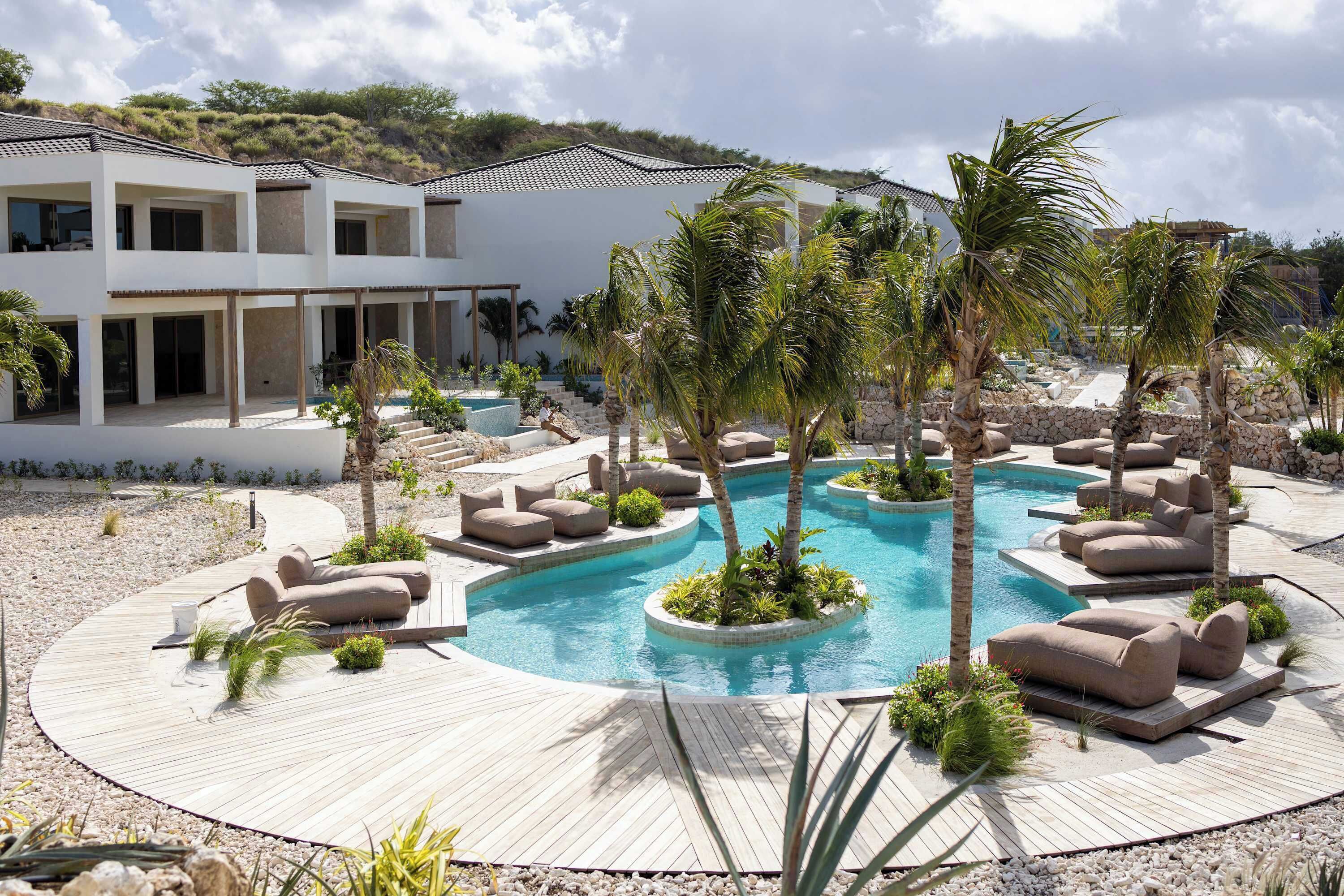 A pool area with lounge chairs and palm trees, surrounded by a modern building with a tiled roof.
