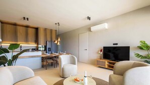 A modern living room with a flat-screen TV, a dining area with a wooden table, and a kitchen with wooden cabinets. - Private Pool Escape - Luminara at The Reef (Sint Michiel)