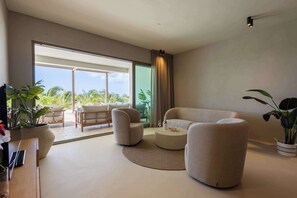 A modern living room with a sofa, armchairs, a coffee table, and a view of a garden through large windows. - The Reef Superior Apartement With Private Pool (Sint Michiel)