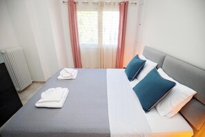 A hotel room with a bed, two pillows, a radiator, and a window with curtains. - Pantheon - A Cozy Nest in the Center of Athens (Athens)