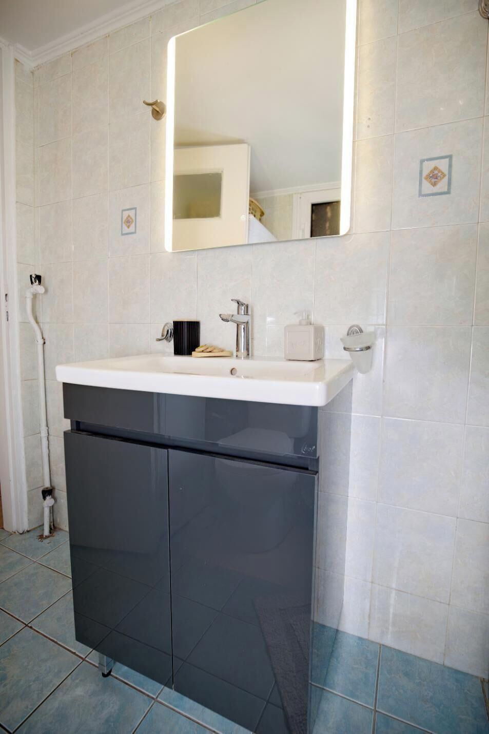 A bathroom with a white sink, dark cabinet, and a mirror above it.