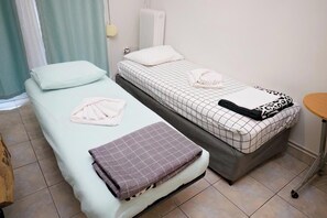A room with two beds, each with a different patterned bedspread, a radiator, and a wooden bench. - Pantheon - A Cozy Nest in the Center of Athens (Athens)