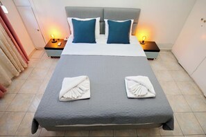 A neatly made bed with two pillows, two bedside tables with lamps, and towels folded on the bed. - Pantheon - A Cozy Nest in the Center of Athens (Athens)