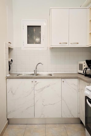 A kitchen with white cabinets, a marble countertop, a built-in microwave, and a sink. - Pantheon - A Cozy Nest in the Center of Athens (Athens)