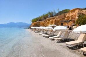 A beach with sun loungers and umbrellas, clear water, and a rocky cliff. - A2 Maisonette - Modern Cretan Living by the Sea (Hersonissos)