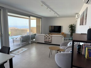 Un salon moderne avec un canapé, une table basse, un téléviseur et un balcon offrant une vue agréable.