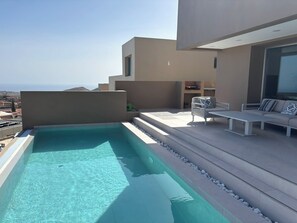 Ein Pool auf dem Dach mit klarem Wasser, eine Sitzgelegenheit mit Tisch und Stühlen sowie ein Blick auf die Stadt.