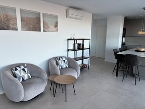 Un salon moderne avec deux fauteuils gris, une petite table en bois et une bibliothèque.