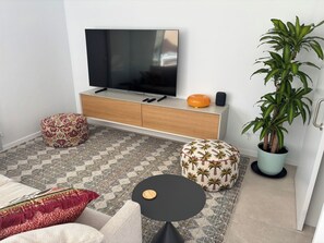 Un salon moderne avec un téléviseur à écran plat, un canapé, une table basse, des poufs à motifs et une plante en pot.