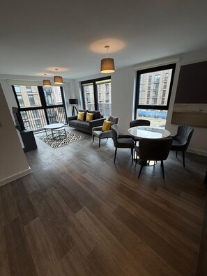 A modern apartment with a dining area, sofa, and large windows. - Stunning 3 Bedroom Apartment-2 Bath with Balcony (Salford)