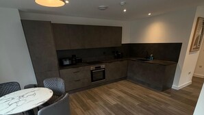 Una cocina moderna con electrodomésticos integrados, una zona de comedor con una mesa de mármol y una silla tapizada en gris.