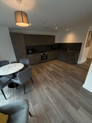 A modern kitchen with built-in appliances, a dining area with a marble table, and a grey upholstered chair. - Stunning 3 Bedroom Apartment-2 Bath with Balcony (Salford)