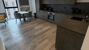 Una cocina moderna con armarios oscuros, horno empotrado y zona de comedor con mesa y sillas.