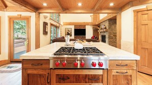 A kitchen with a central island, wooden cabinetry, a stone fireplace, and a large window. - 6BR Deer Valley retreat with hot tub, game room, and mountain views. (Park City)