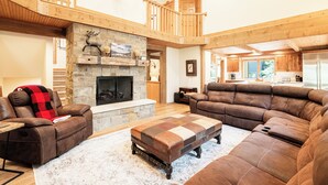 A spacious living area with a stone fireplace, leather sofas, and a wooden staircase. - 6BR Deer Valley retreat with hot tub, game room, and mountain views. (Park City)