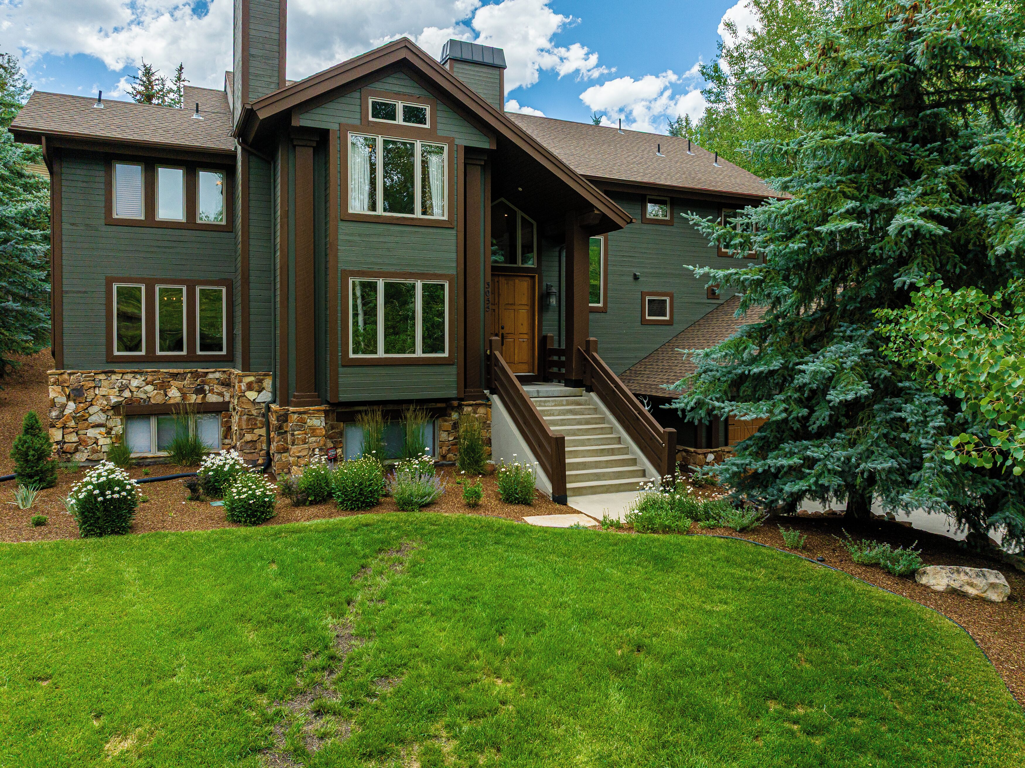 A two-story house with a stone foundation, a wooden staircase, and a well-maintained lawn.