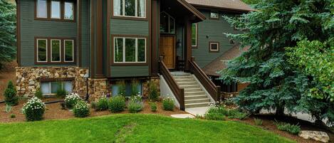 A two-story house with a stone foundation, a wooden staircase, and a well-maintained lawn.