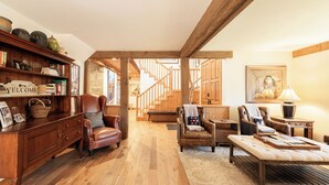 A spacious living area with a wooden reception desk, leather armchairs, a sofa, and a staircase leading to an upper level. - 6BR Deer Valley retreat with hot tub, game room, and mountain views. (Park City)