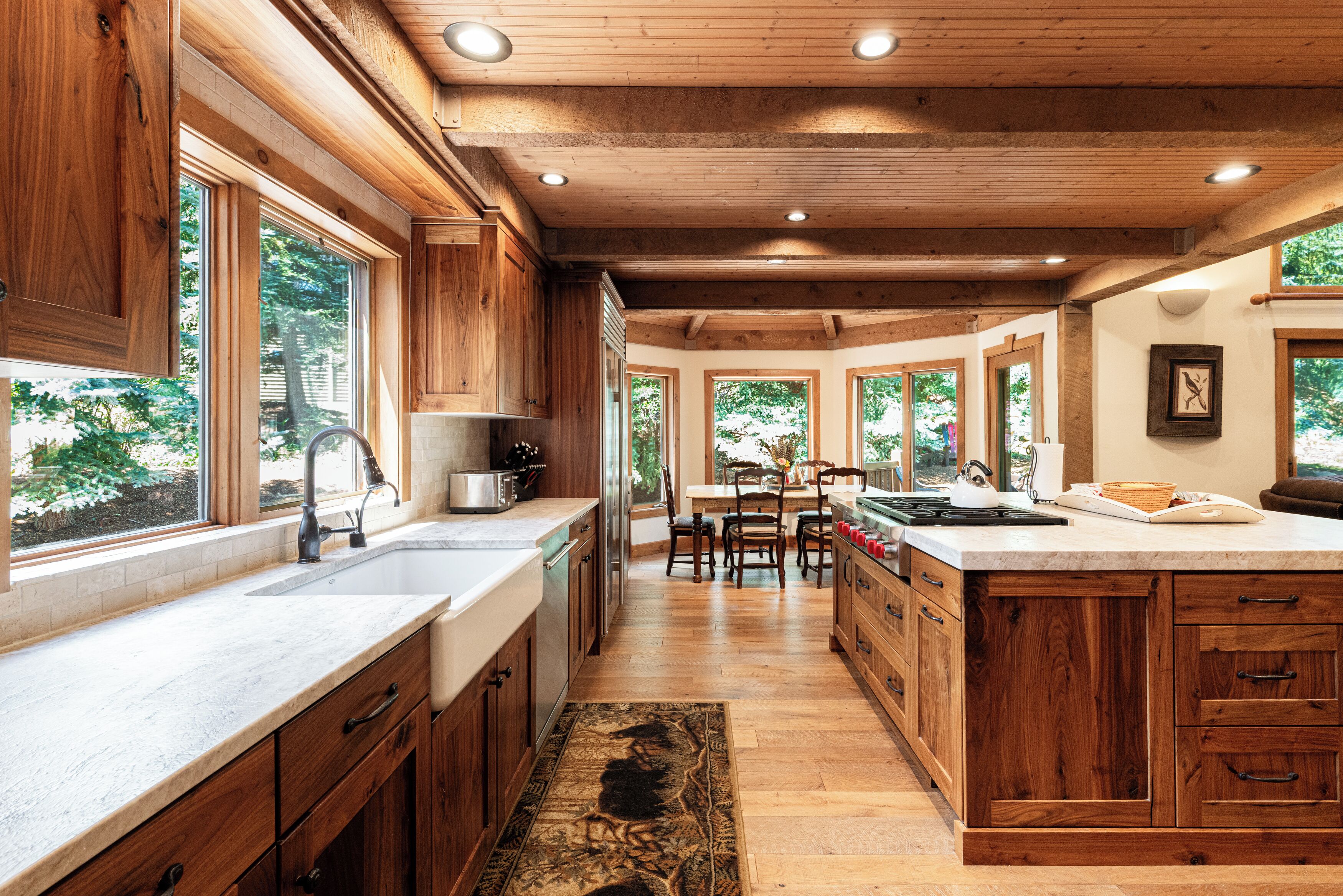 A modern kitchen with wooden cabinetry, a large island, and a view of the outdoors through multiple windows.
