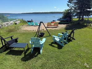 Een gazon met een schommel, Adirondack stoelen en uitzicht op een meer.