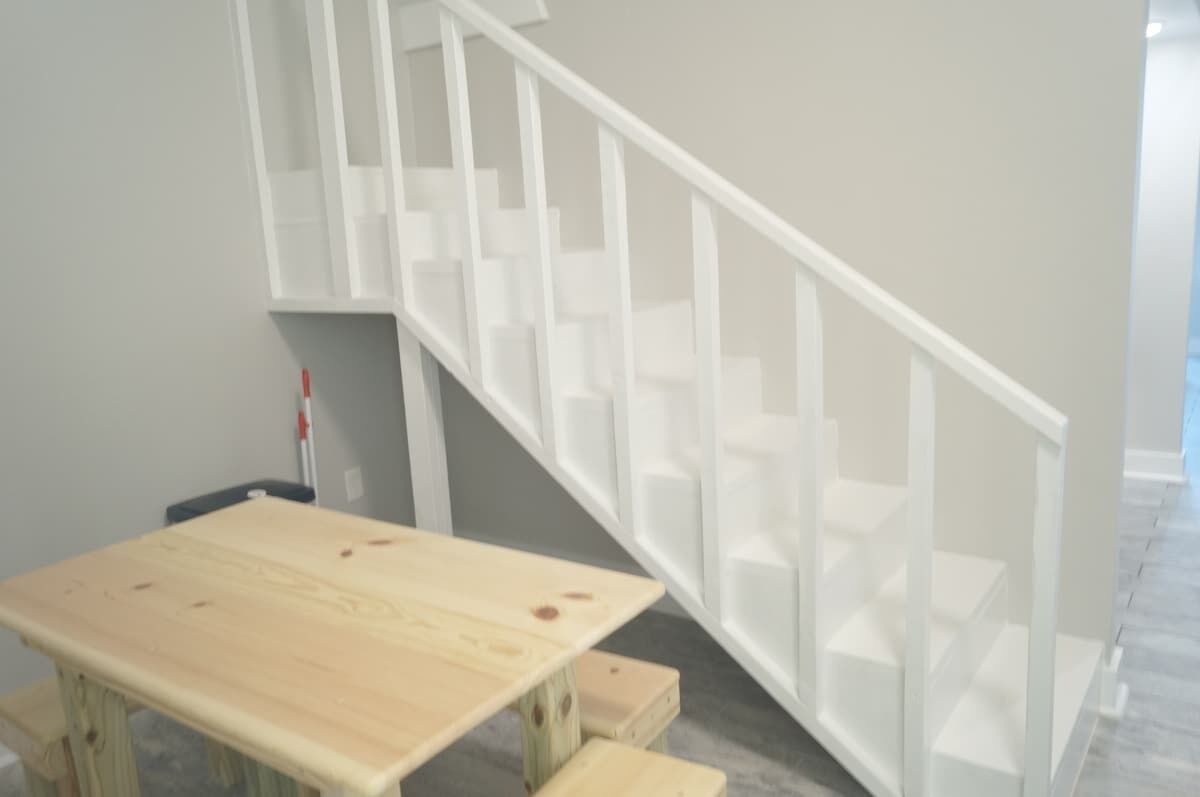 Una escalera con barandas blancas y una mesa de madera con una silla.