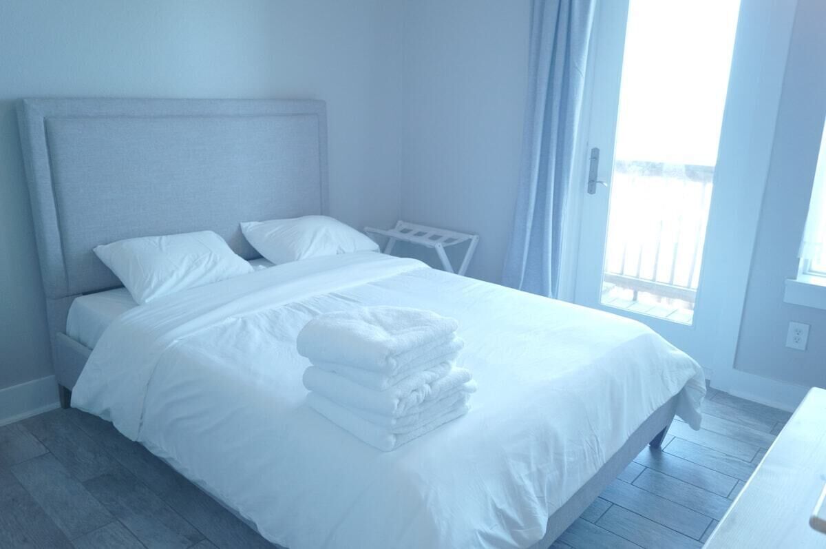 A hotel room with a bed, a bedside table, and a view of the outdoors.