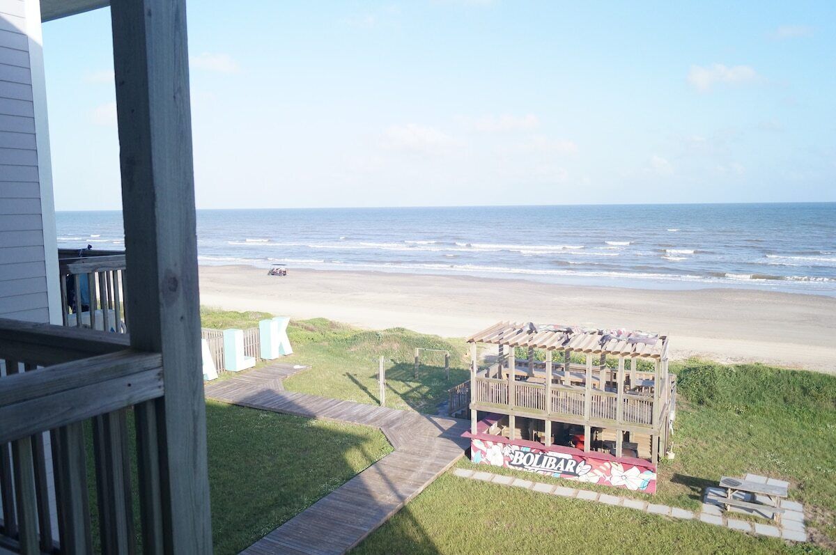 Vista a la playa desde una terraza de madera, con un edificio con el rótulo 'BOLIBAR' en primer plano.