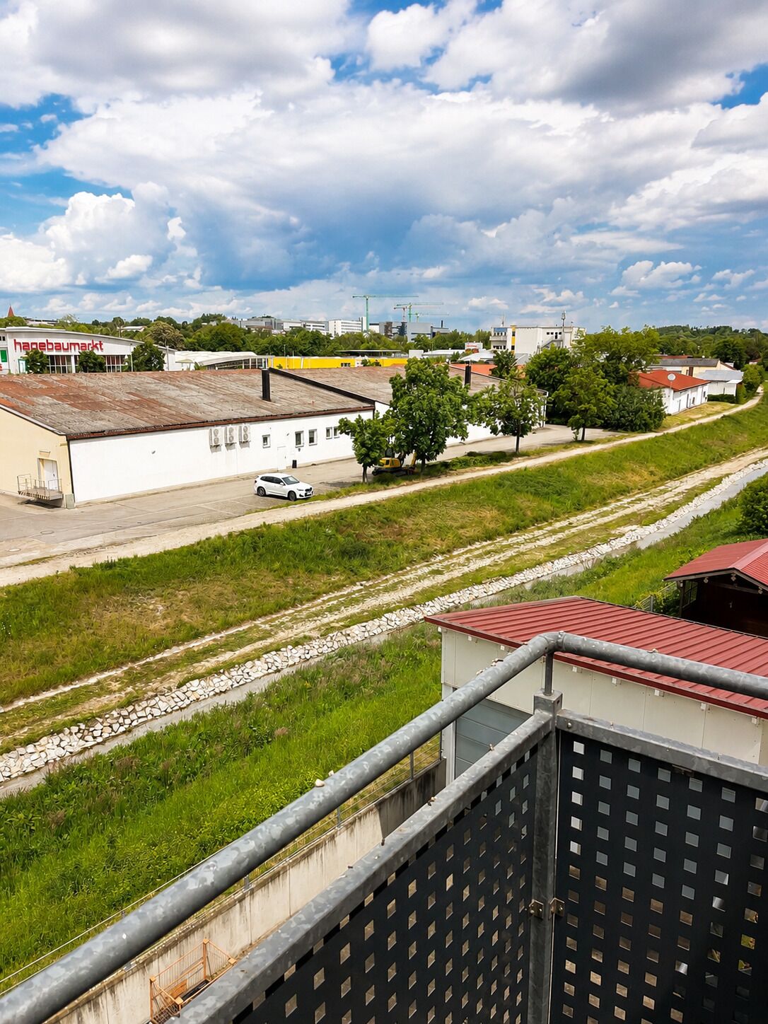 A view of a building with a red roof, a white building with a sign, and a paved area with a car.