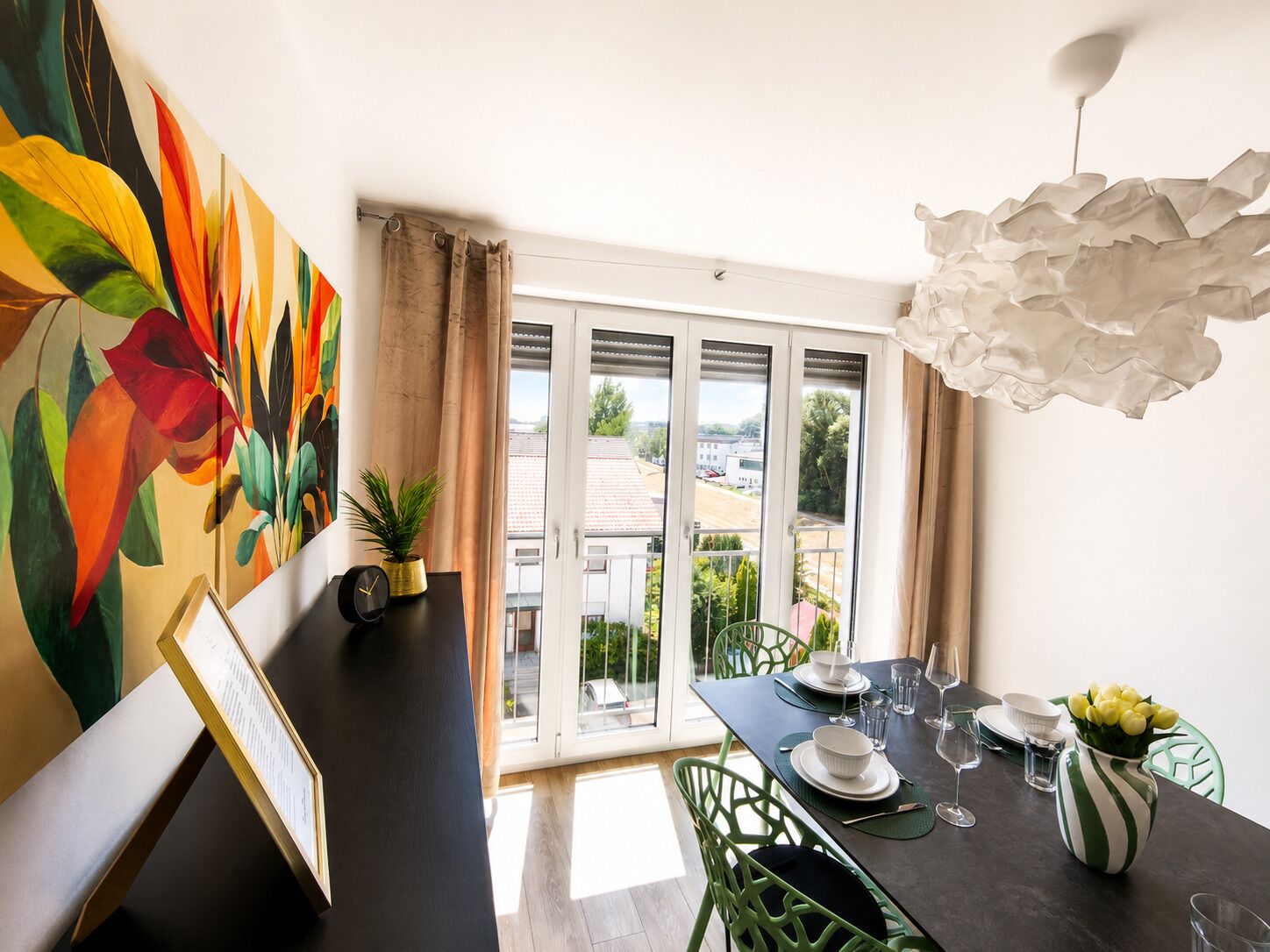 A dining area with a table set for two, a potted plant, and a painting on the wall.