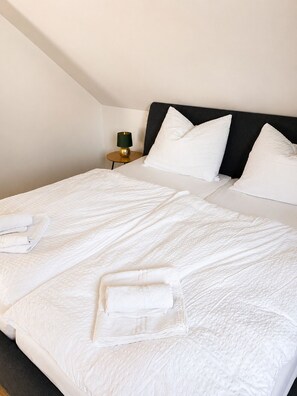 A neatly made bed with white linens and pillows, a small bedside table with a lamp, and a dark headboard. - Premium Apartment - 90 m² - Central, near City Park (Pfaffenhofen an der Ilm)