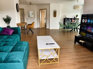 A modern living room with a teal sofa, a white coffee table, and a TV displaying streaming apps. - Premium Apartment - 90 m² - Central, near City Park (Pfaffenhofen an der Ilm)