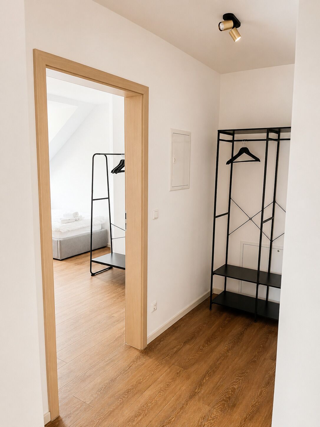 Ein Zimmer mit Holzboden, einem schwarzen Metallschrank und einem Bett mit grauem Kopfteil.