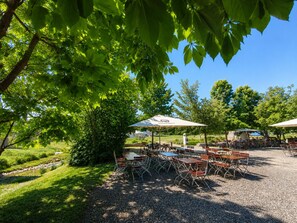 An outdoor seating area with tables and chairs under umbrellas, surrounded by trees and a gravel path. - Premium Apartment - 90 m² - Downtown, near the city park (Pfaffenhofen an der Ilm)