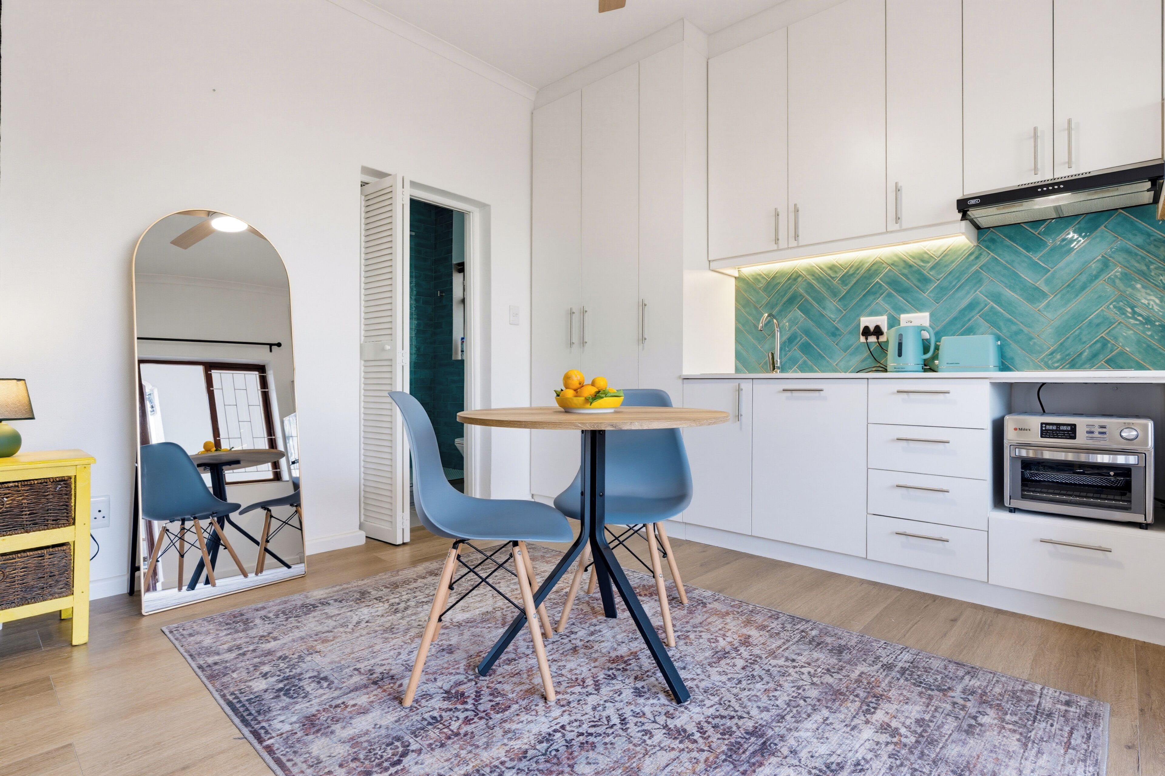 Eine moderne Küche mit weißen Schränken, einer Fischgrät-Spritzschutzleiste, einem runden Tisch mit Stühlen und einem eingebauten Backofen.