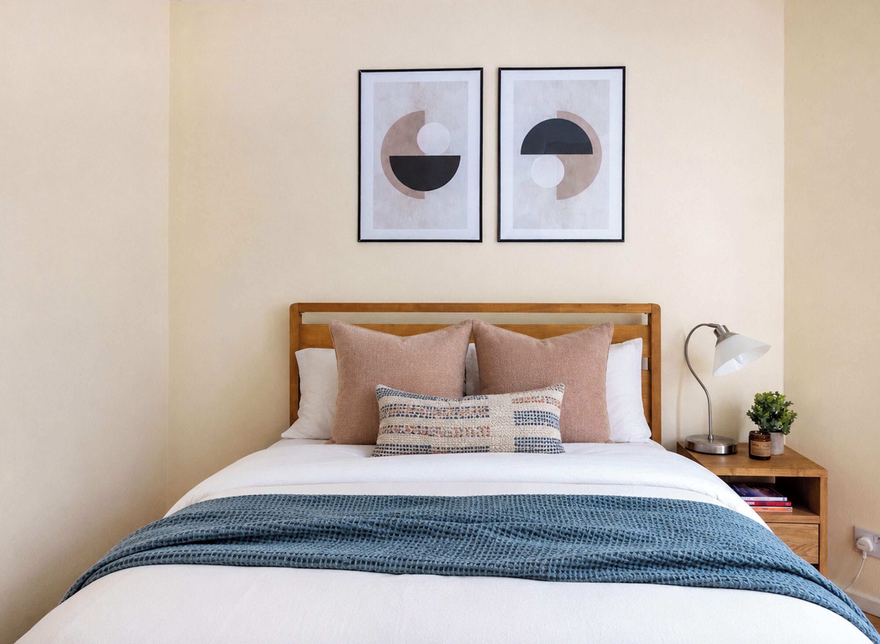 Una cama bien hecha con una colcha azul, un cabecero de madera y dos cuadros en la pared.