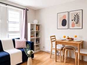 A modern living room with a blue sofa, a dining table with chairs, a bookshelf, and two framed artworks on the wall. - Edinburgh Gem Near Castle & Old Town (Edinburgh)