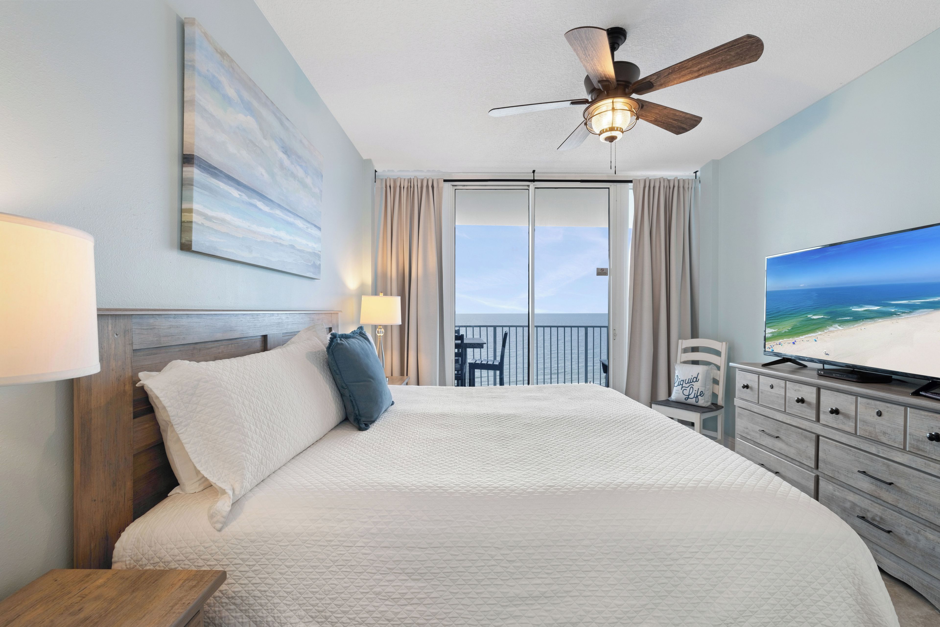 Ein Hotelzimmer mit Bett, Deckenventilator, Fernseher und Blick auf den Strand.