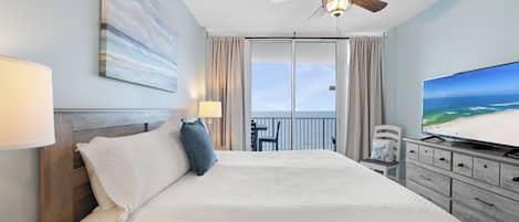 Ett hotellrum med en säng, en takfläkt, en tv och utsikt över stranden.