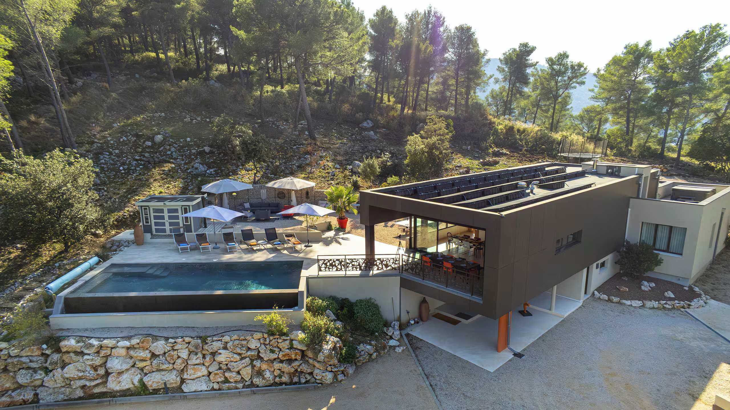 A modern house with a swimming pool, outdoor seating, and a view of the surrounding forest.