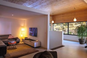 A modern living room with a flat-screen TV, a sofa, a coffee table, and a large window with a view of trees. - Villa Horizona in G Menos (Gemenos)