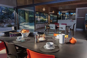 A modern dining area with a table set for two, including plates, cups, and a croissant basket. - Villa Horizona in G Menos (Gemenos)