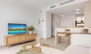 Ein modernes Wohnzimmer mit Fernseher, ein Essbereich mit Tisch und Stühlen sowie eine Küche im Hintergrund.